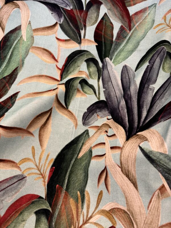 Close-up of a Pierre Frey printed velvet with large tropical leaves in green, plum, salmon and red on a pale blue-grey ground