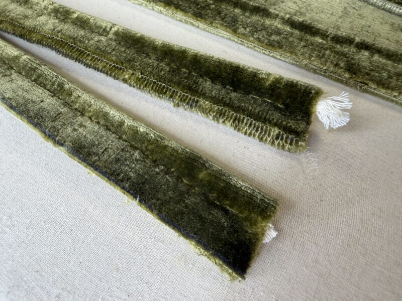 Strips of single piping made in olive green velvet, with the white piping cord visible at the ends, laid on a work table